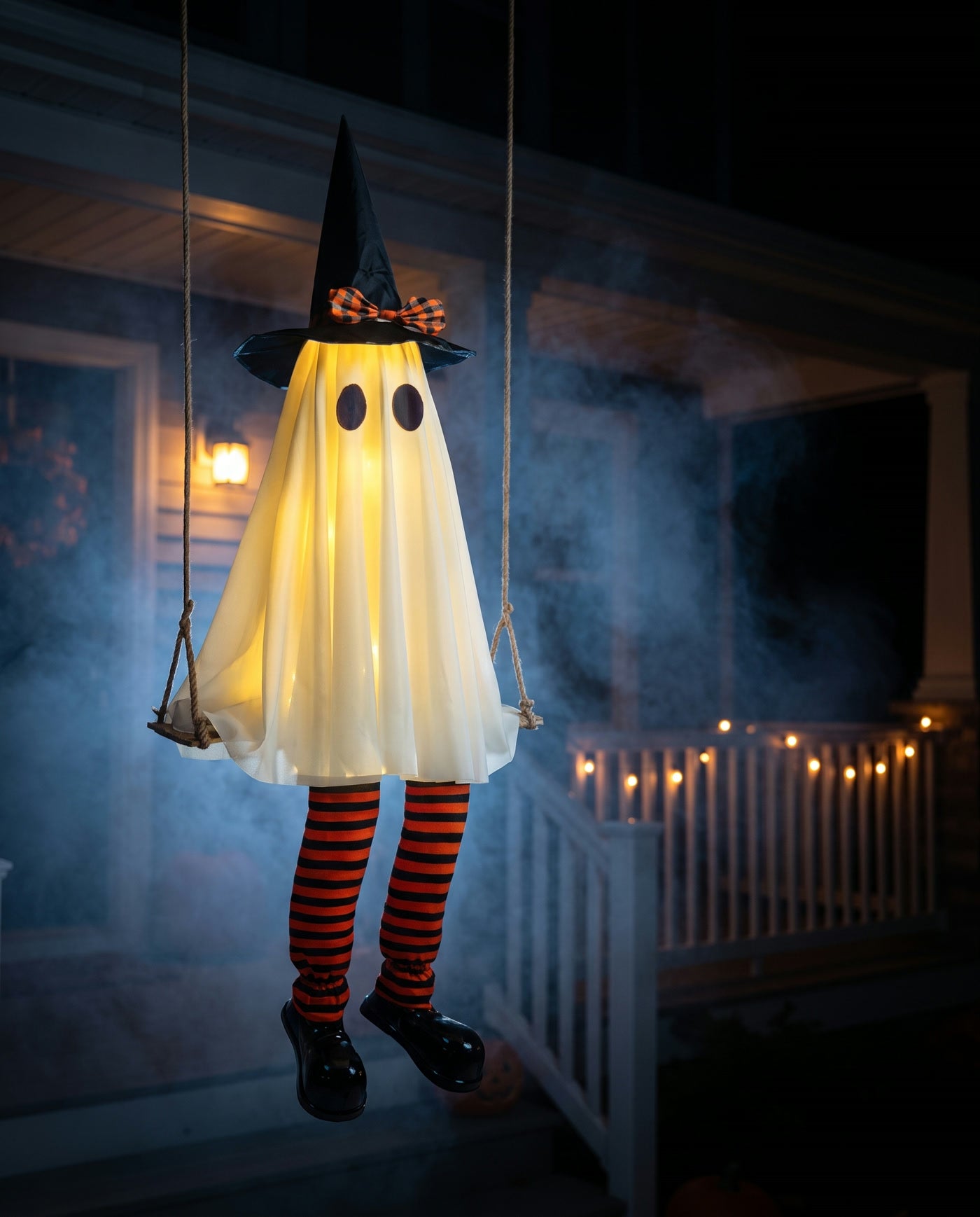 A glowing ghost in a witch hat hanging from a rope swing on a dark porch