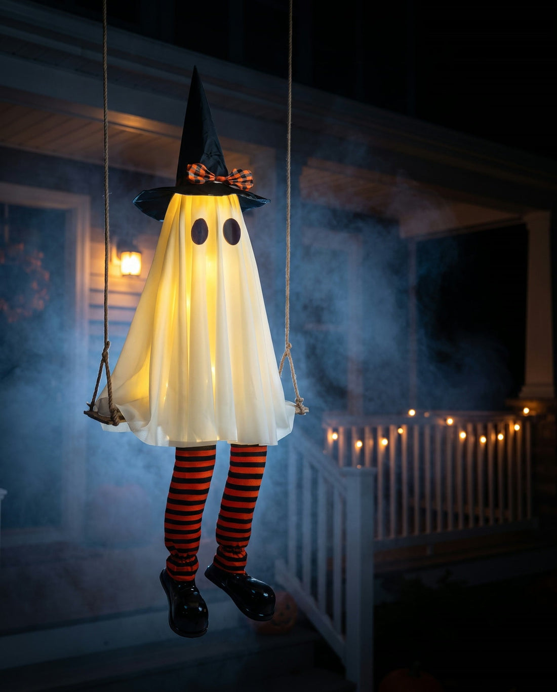 A glowing ghost in a witch hat hanging from a rope swing on a dark porch